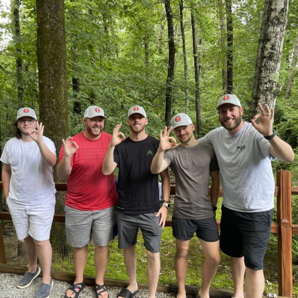 Five men wearing hats with the Athens Scuba logo posing in front of a fence in the woods