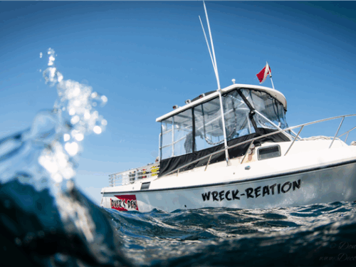 A small boat named Wreck-Reation in the water with a small wave coming at the camera