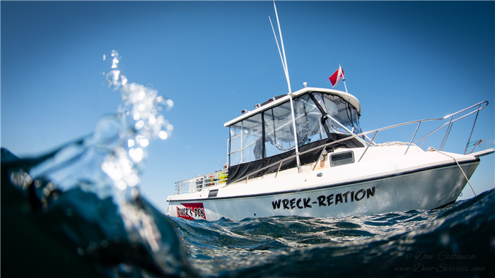 A small boat named Wreck-Reation in the water with a small wave coming at the camera